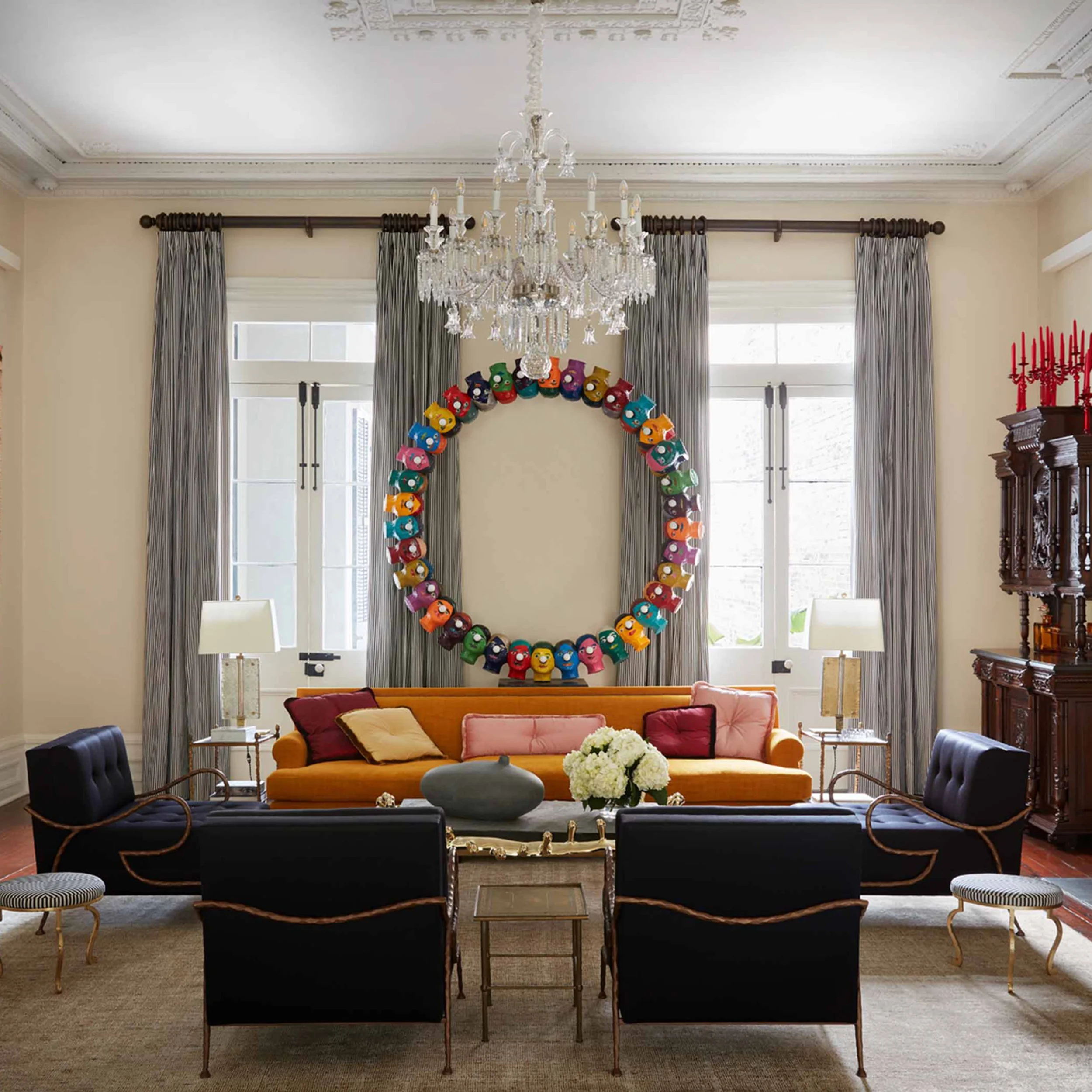 Eclectic living room interior by Shawn Henderson Interior Design featuring an orange sofa, black armchairs, and a large sculptural wall wreath.