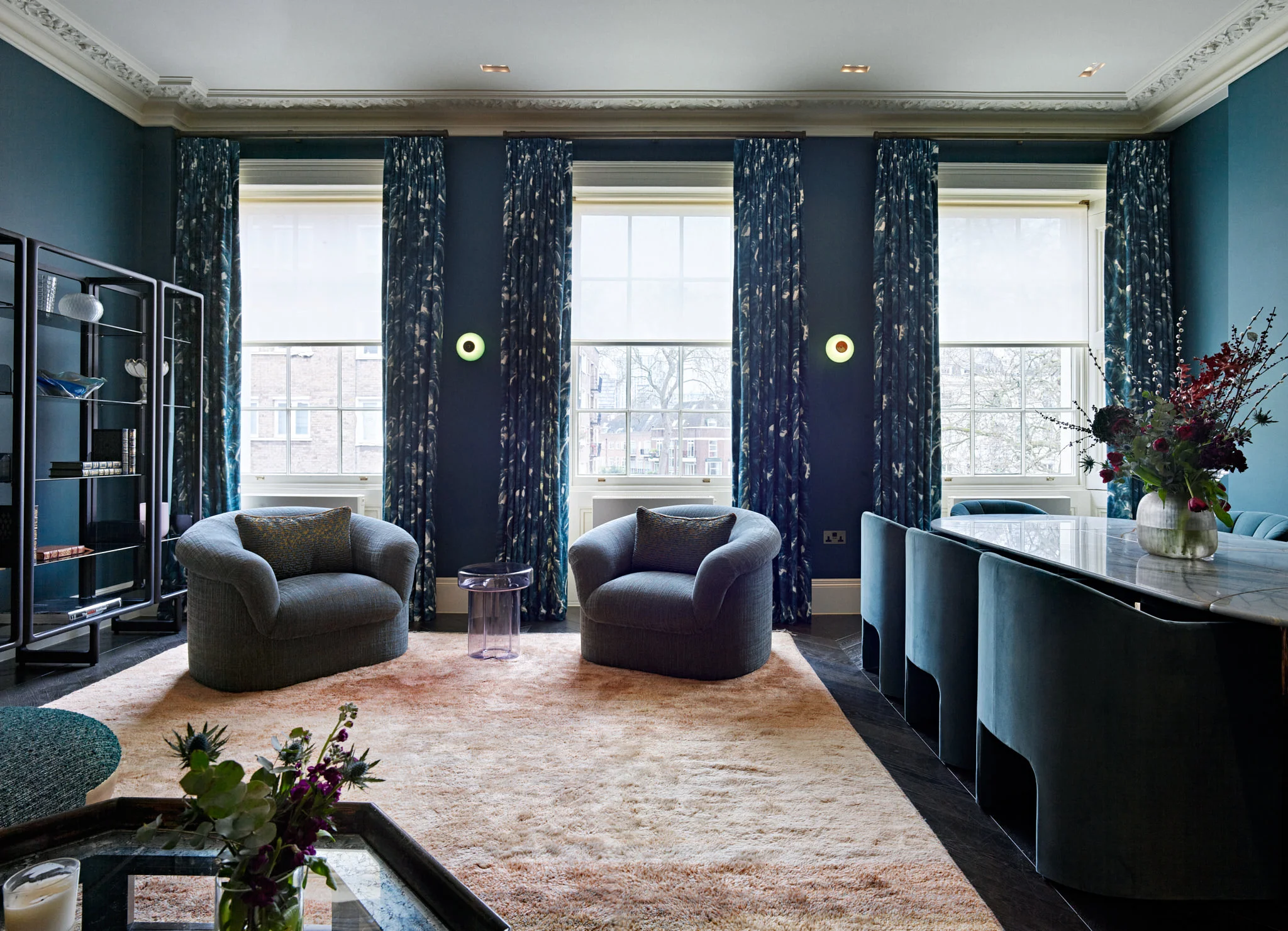 Luxurious living and dining room with deep teal walls, patterned blue curtains, and rounded armchairs by Carden Cunietti for Hyde Park.