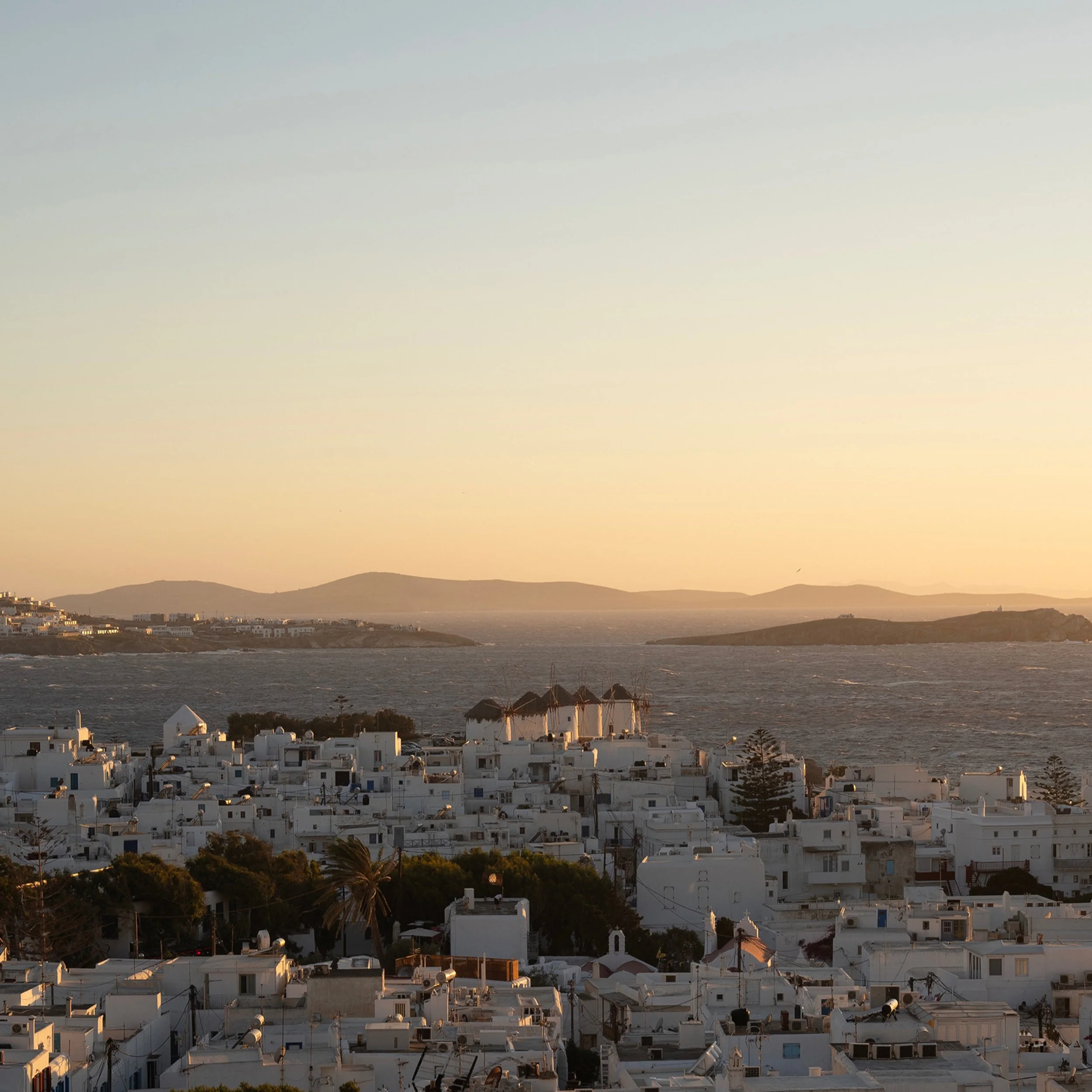 High-angle view of whitewashed Mykonos town architecture overlooking the sea at sunset by Pirajean Lees.