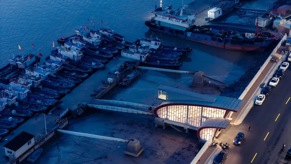 Aerial view of a waterfront cinema building with a curved metal roof and illuminated facade by TheY architects at dusk.