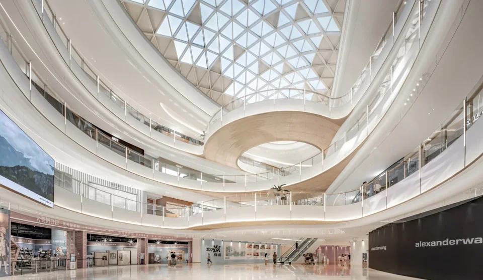 Multi-level commercial atrium with curved white balconies and a triangular diagrid glass skylight by AICO.
