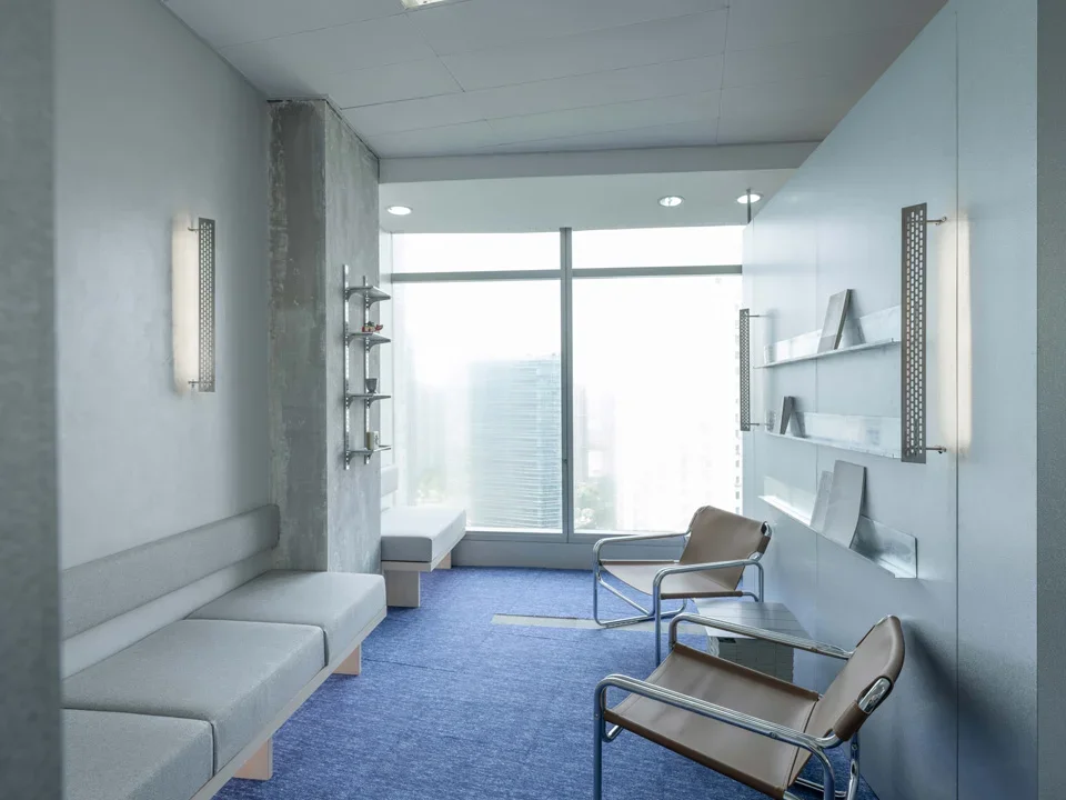 Interior waiting lounge with blue carpet, leather armchairs, and perforated metal wall sconces by All Design Studio.