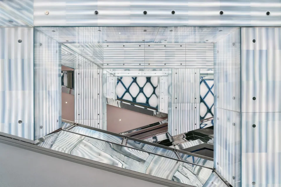 Translucent fluted glass panel cladding and reflective steel elements framing an interior atrium view by All Design Studio.