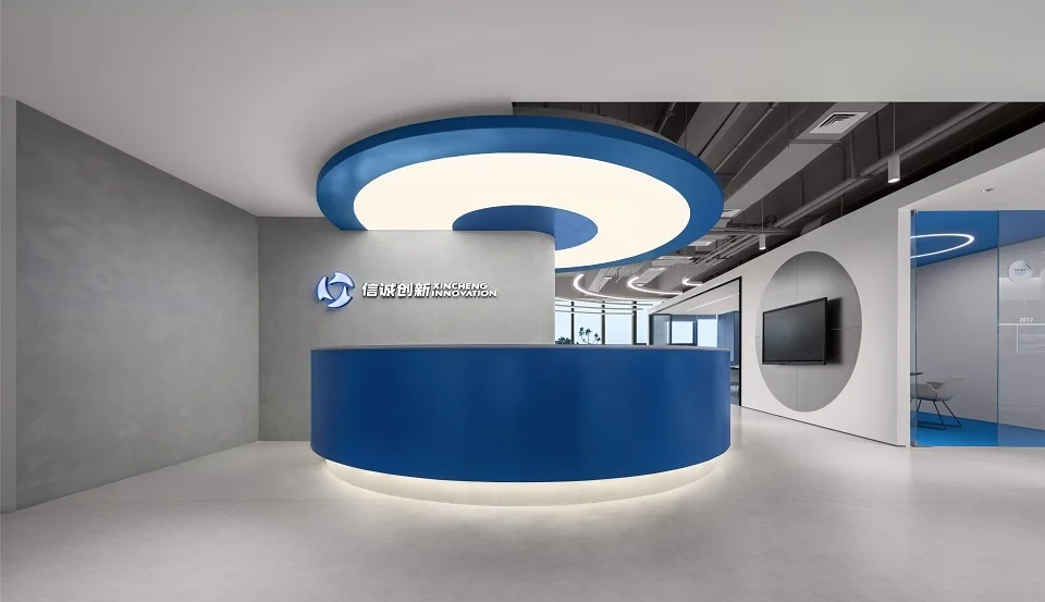 Modern corporate reception desk with a curved blue counter and matching circular illuminated ceiling element, set against gray textured walls.