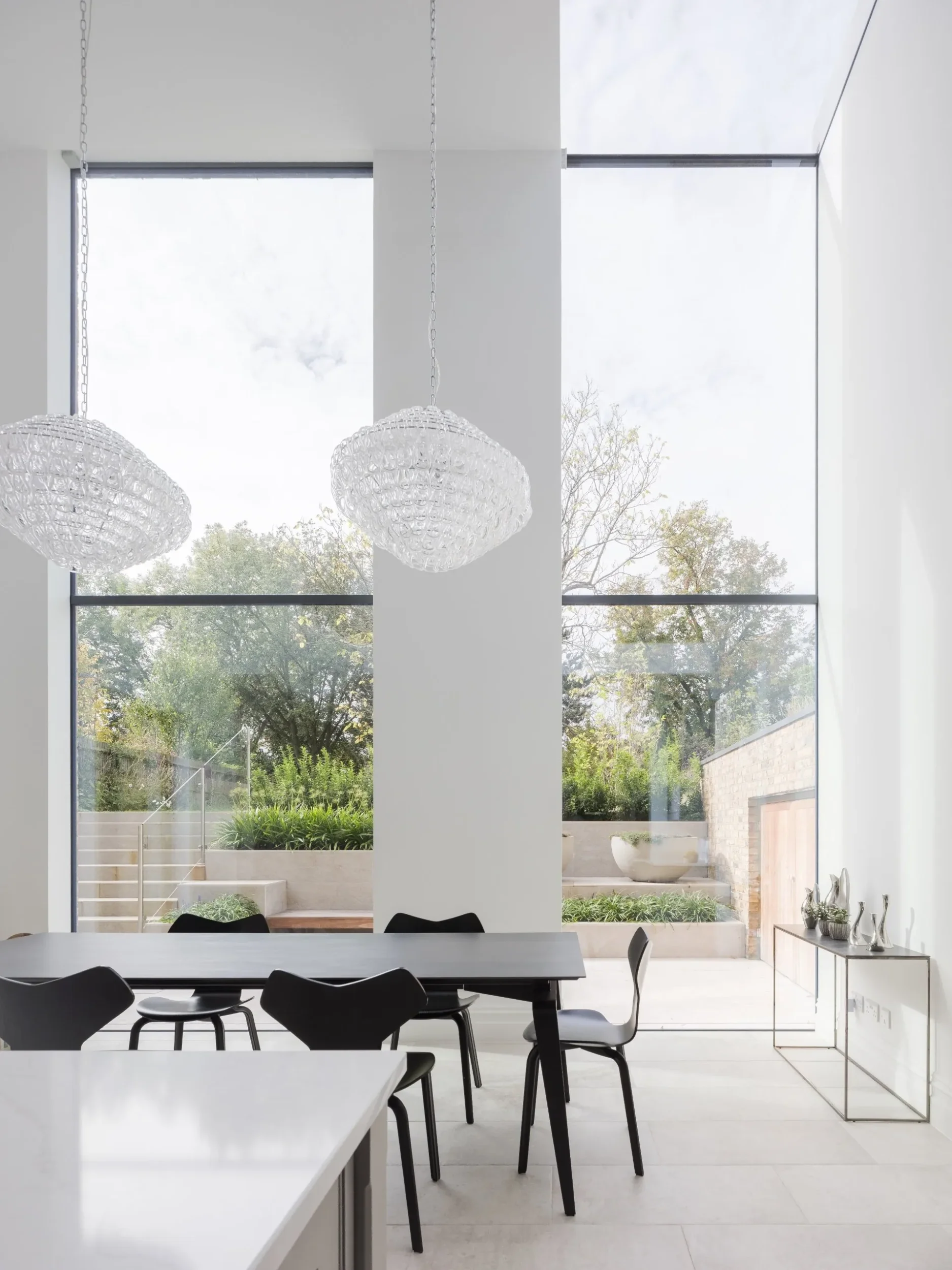 Double-height dining space with floor-to-ceiling windows and large glass pendant lights by RDA Architects.