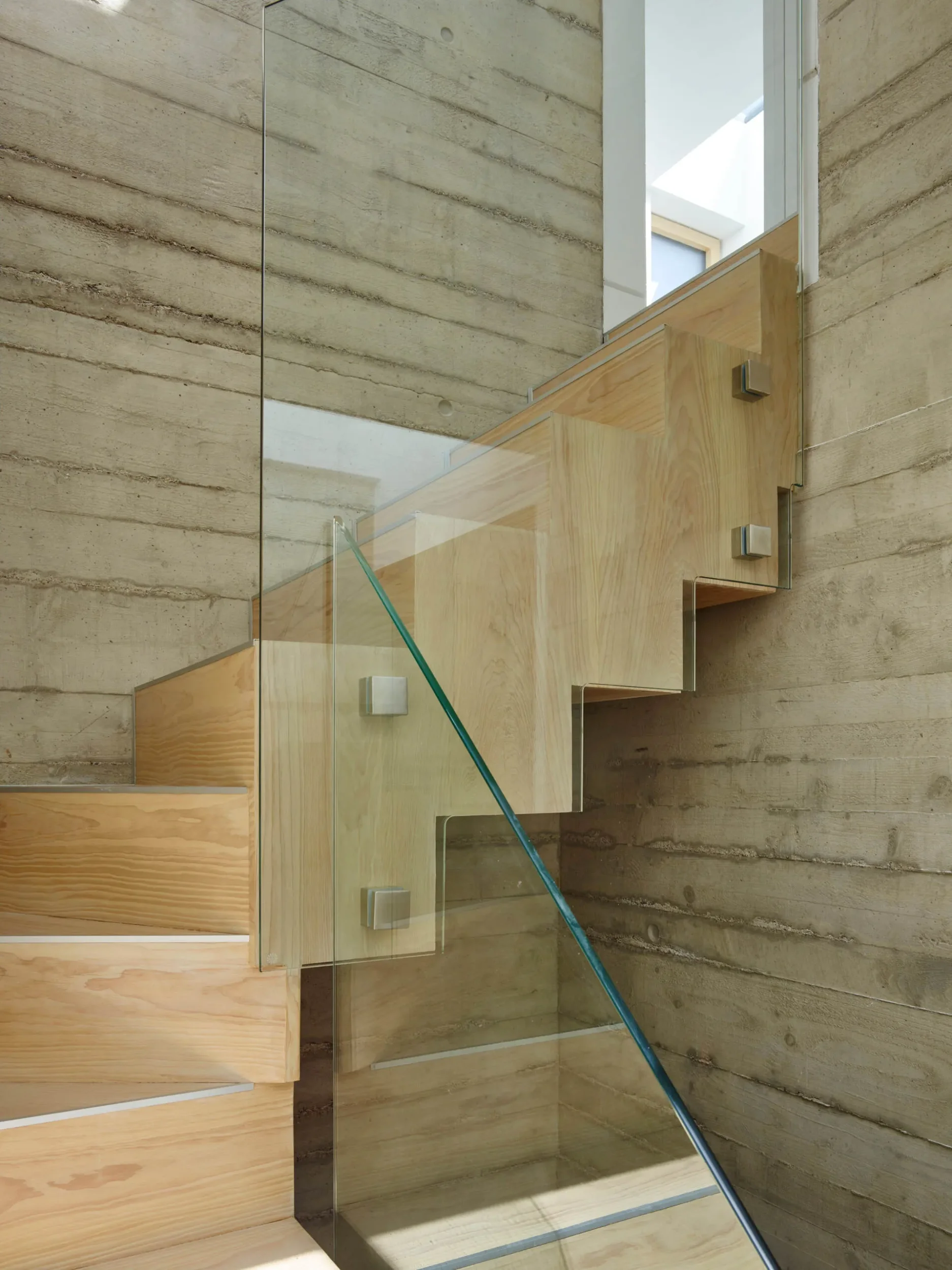 Interior stair with exposed board-formed concrete walls, timber treads and risers, and frameless glass balustrade by RDA Architects.