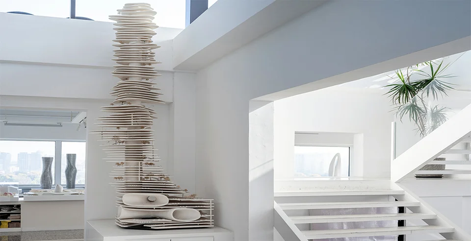 Interior of MAD Office in Beijing featuring a tall architectural tower model with stacked floor plates and a white staircase.