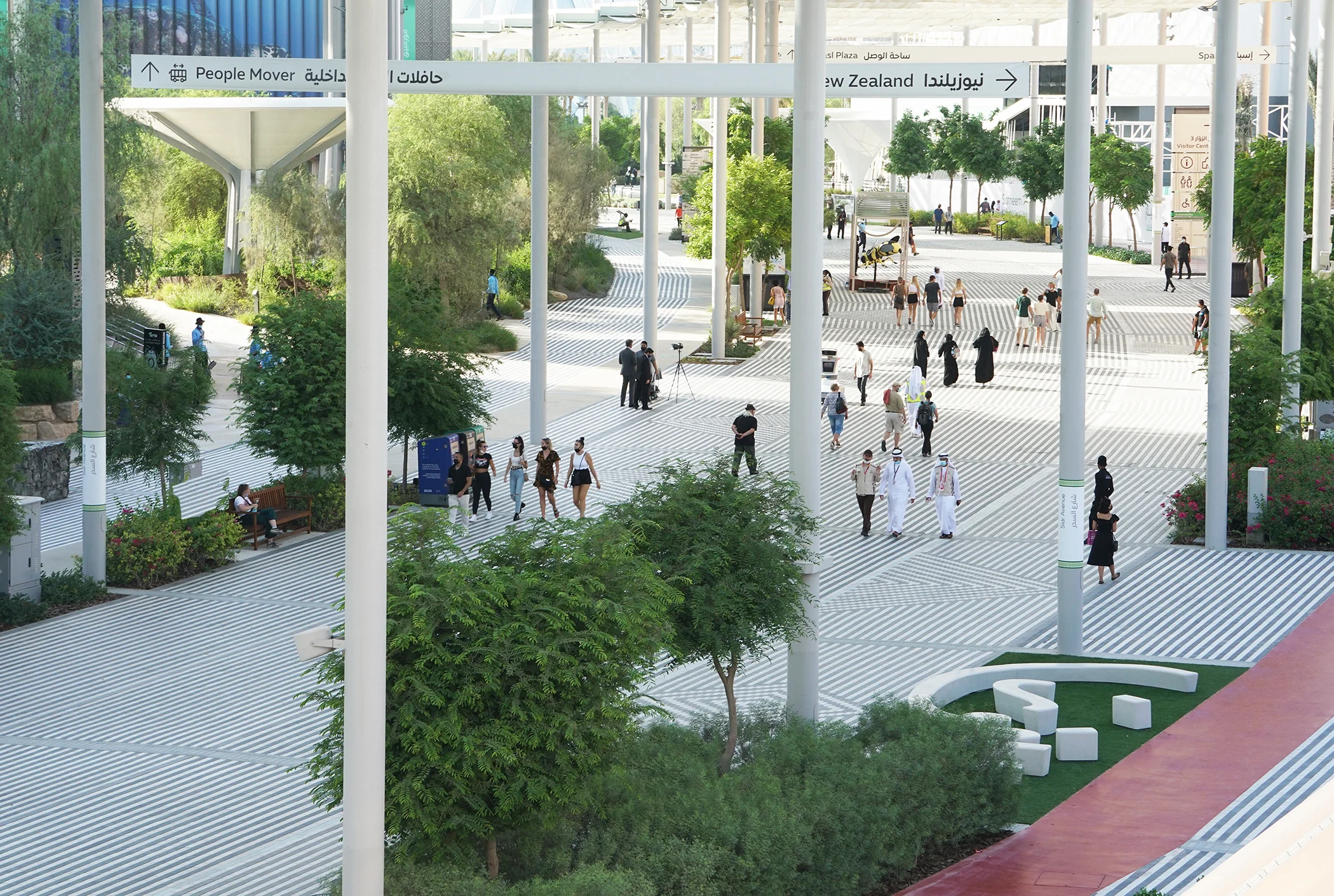 Elevated view of a shaded pedestrian concourse with striped paving and slender columns by Asif Khan Studio at Expo 2020 Public Realm.