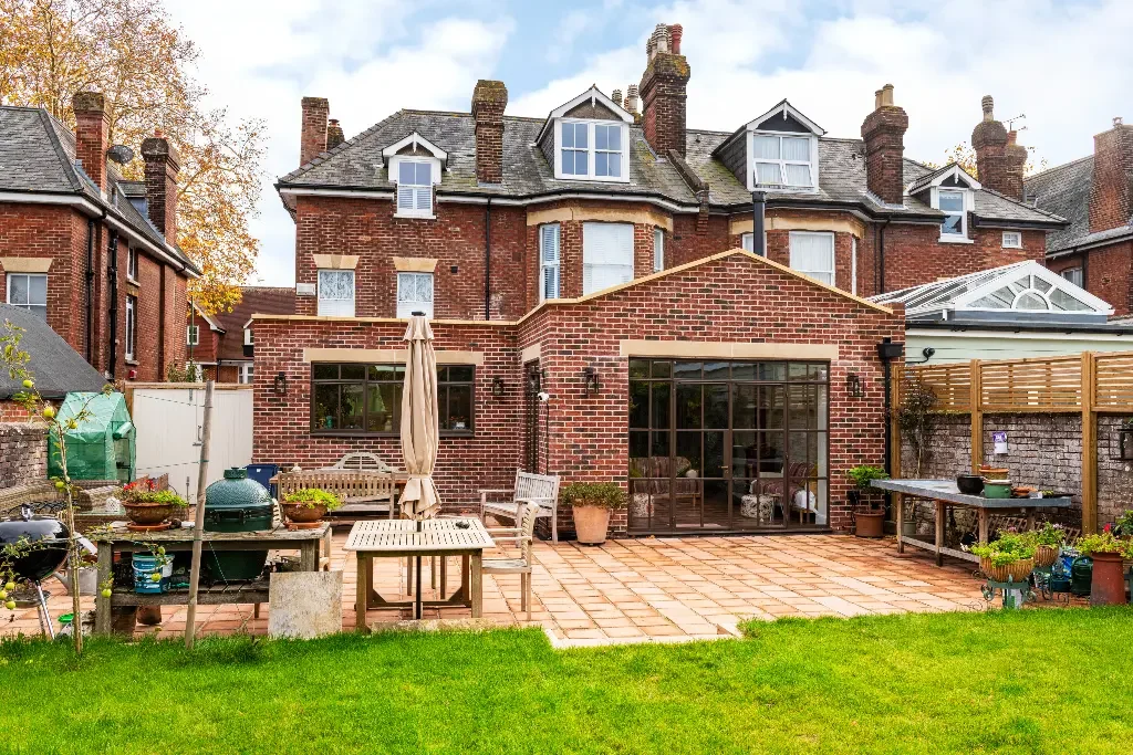 Rear red brick extension on a Victorian house with dark framed glazing opening to a paved patio by James Clague Architects.