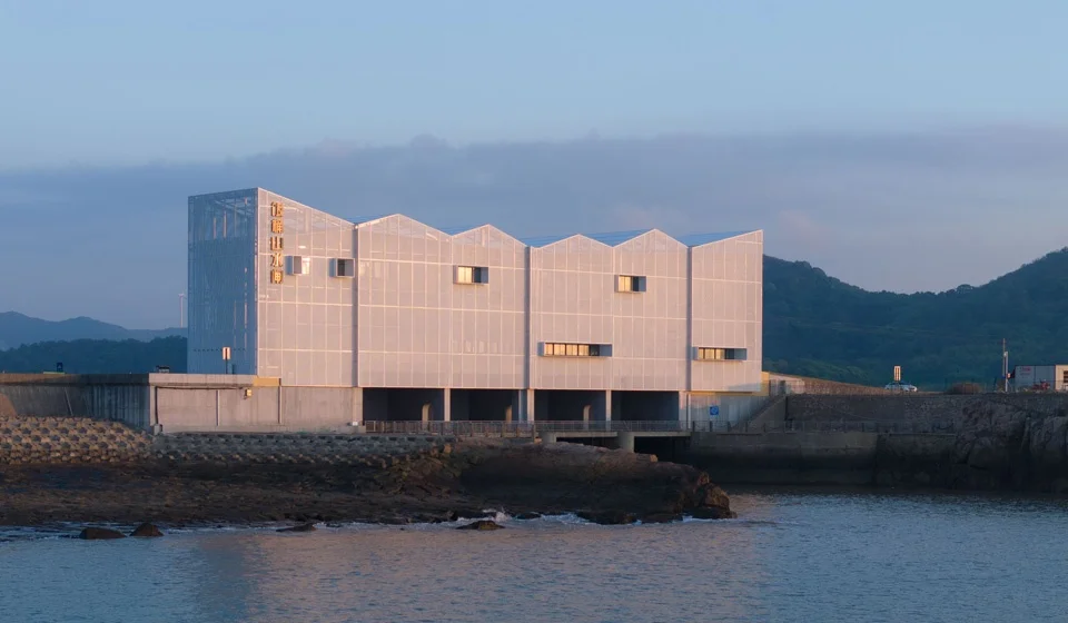 Coastal industrial building with perforated metal skin and sawtooth roof profile by MARS Studio.