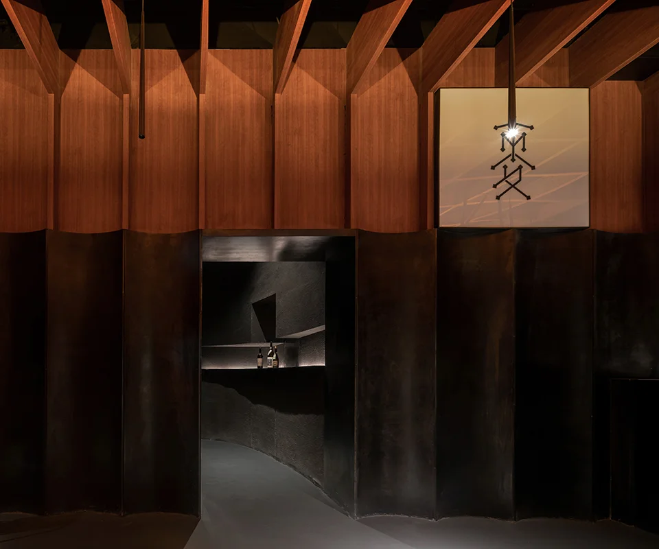 Dark interior bar threshold with pleated metal lower wall, timber fin ceiling, and a glowing branded signage box by 大舟建筑设计事务所 in Shanghai.