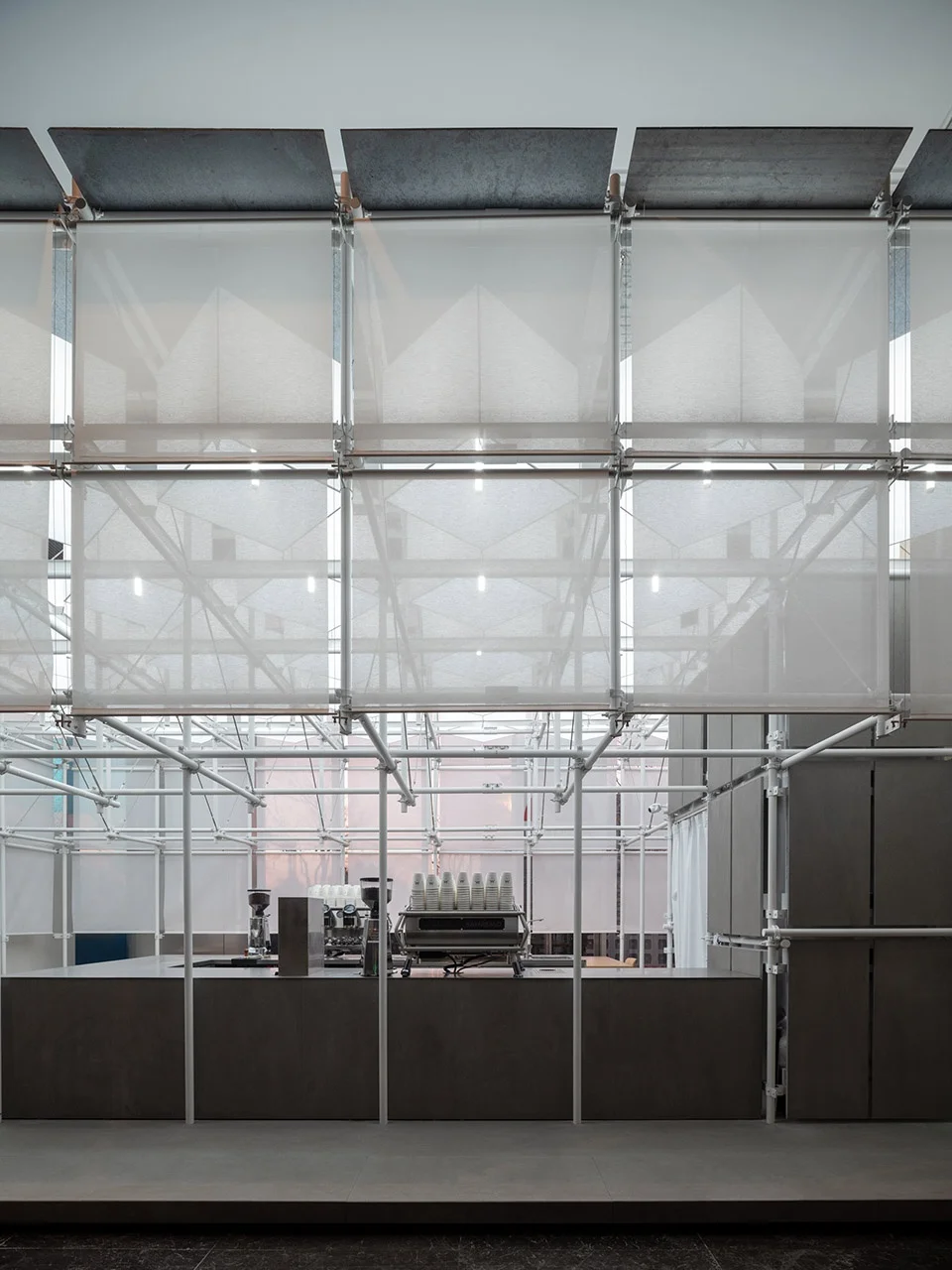 Interior cafe counter framed by a modular tubular steel scaffolding system and translucent fabric panels.
