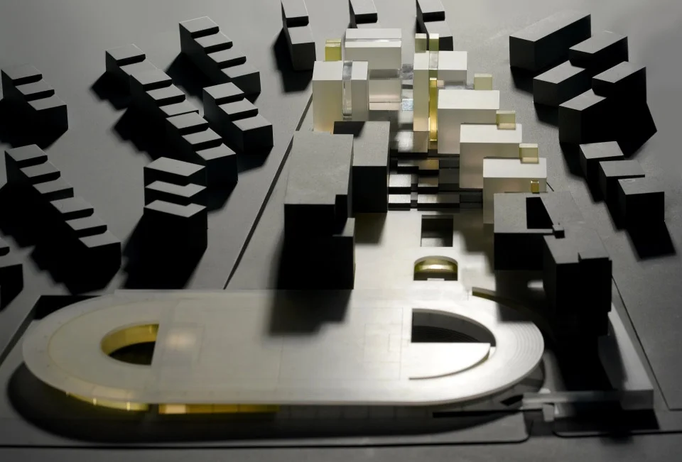 Physical architectural massing model of a school campus expansion showing dark and white volumes set on a dark site base.