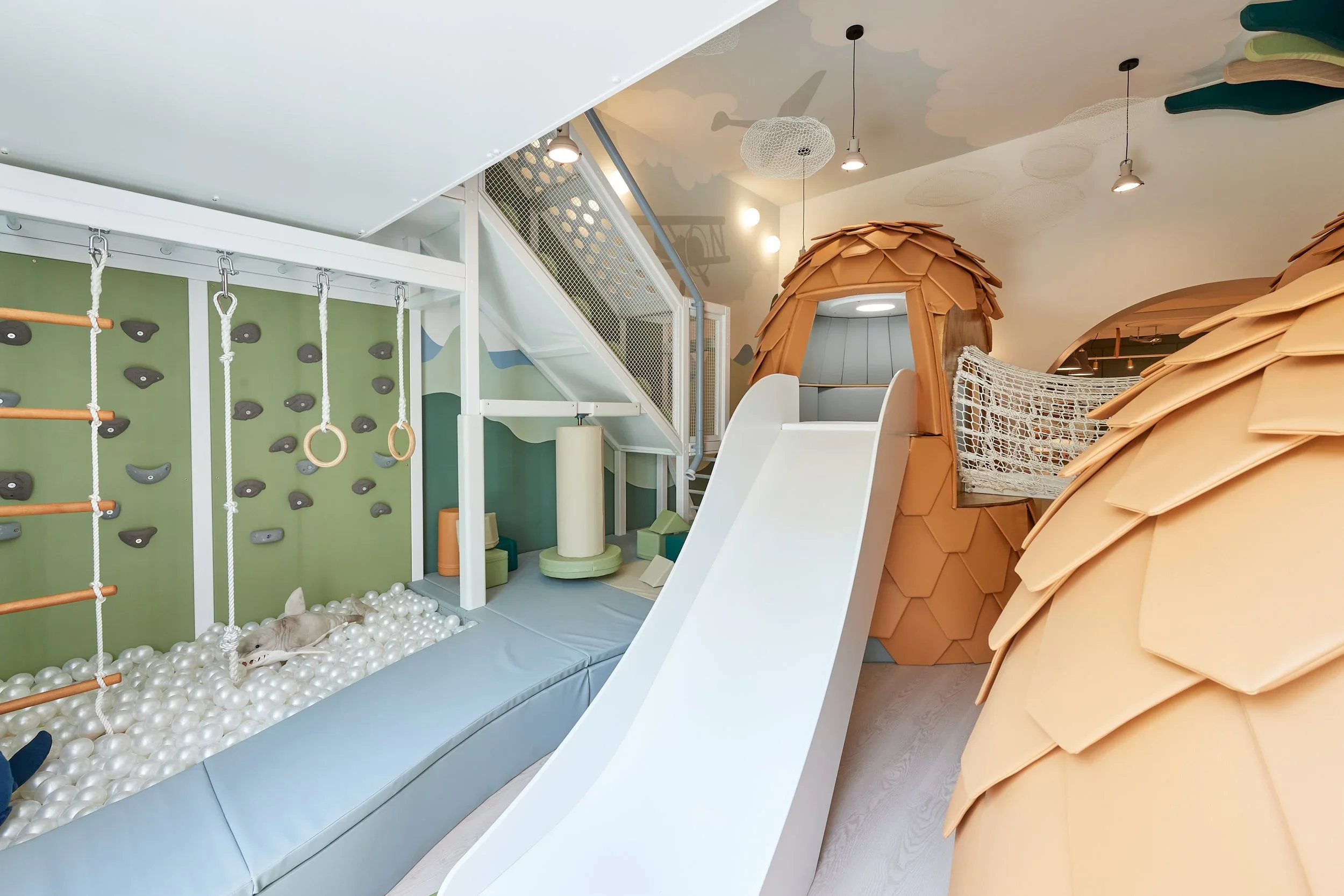 Indoor children playroom interior with climbing wall, ball pit, slide, and custom play pods by Simpson Studio Architects.
