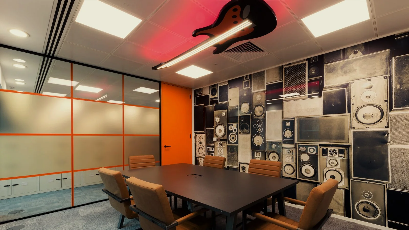 Meeting room with speaker-graphic wall mural, orange acoustic paneling, and custom guitar light fixture by Niche Projects London.