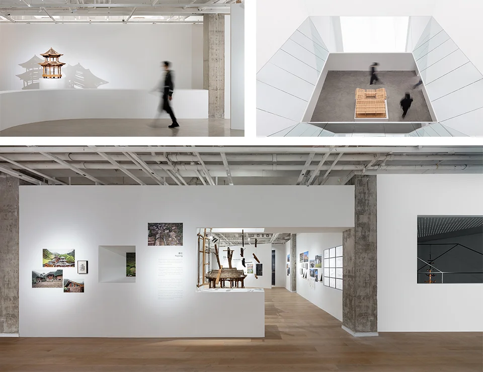 Exhibition interior views showing white gallery walls, exposed concrete columns, wooden model displays, and wood flooring.