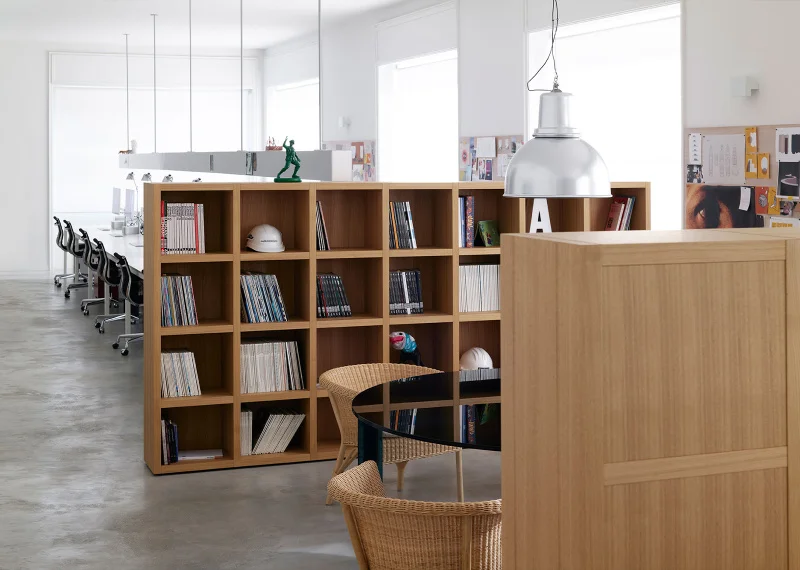 Bright open-plan office interior by Lissoni featuring timber bookcases as spatial dividers and polished concrete floors.