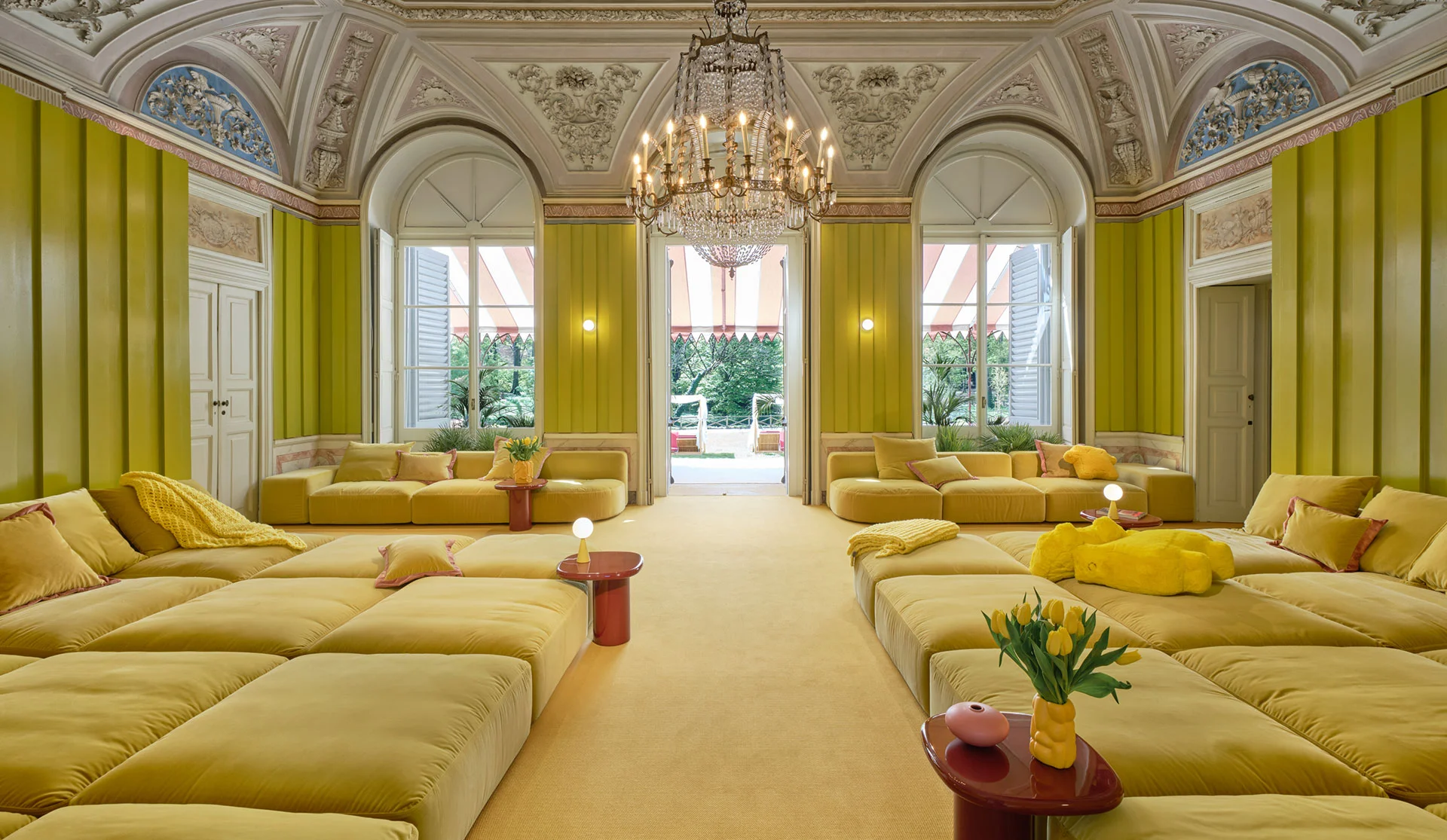 Symmetrical grand interior with chartreuse wood-paneled walls, ornate historic molded ceilings, and modular yellow seating by Matteo Thun & Partners.