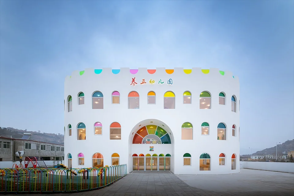 Curved white facade of a kindergarten building with colorful arched windows and a large arched rainbow entrance.