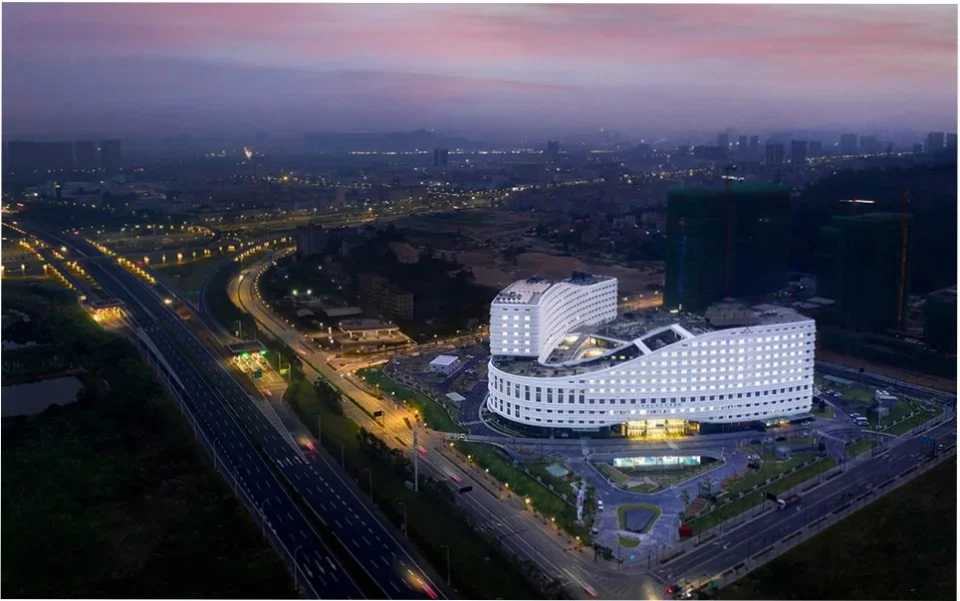Aerial twilight view of a large curved white institutional or hospital complex by AIA Life Designers.