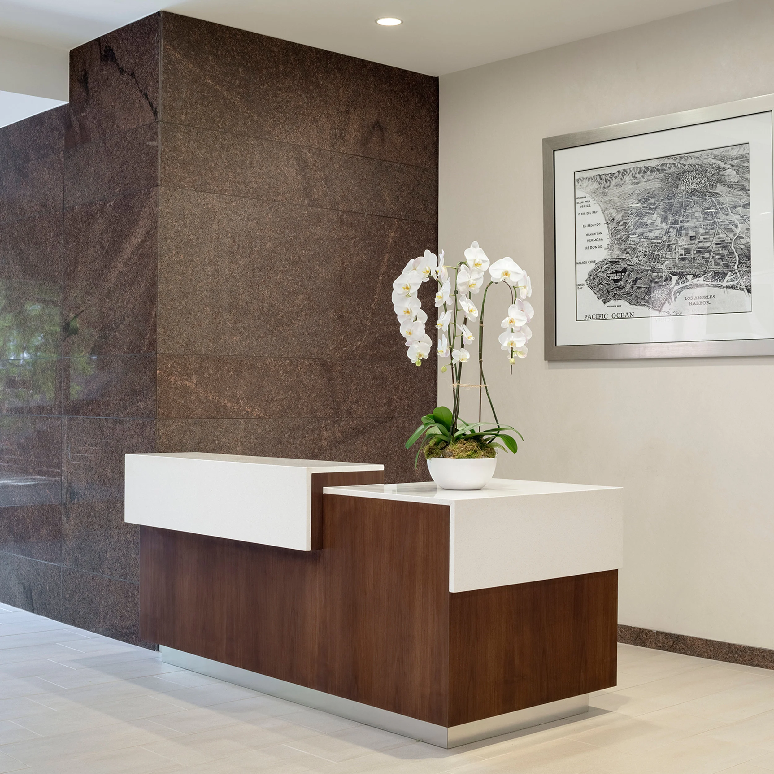 Reception desk with wood and white quartz top, backed by a polished brown granite column and framed map by Rivers & Christian.