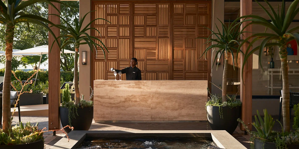 An outdoor bar with a stone counter and geometric timber screen wall by David Collins Studio.