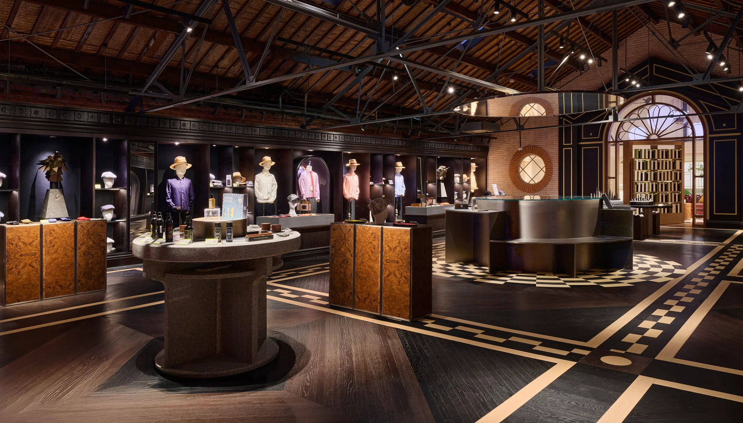 Interior of a retail boutique by Shed featuring dark wood herringbone flooring, exposed steel roof trusses, and custom display fixtures.