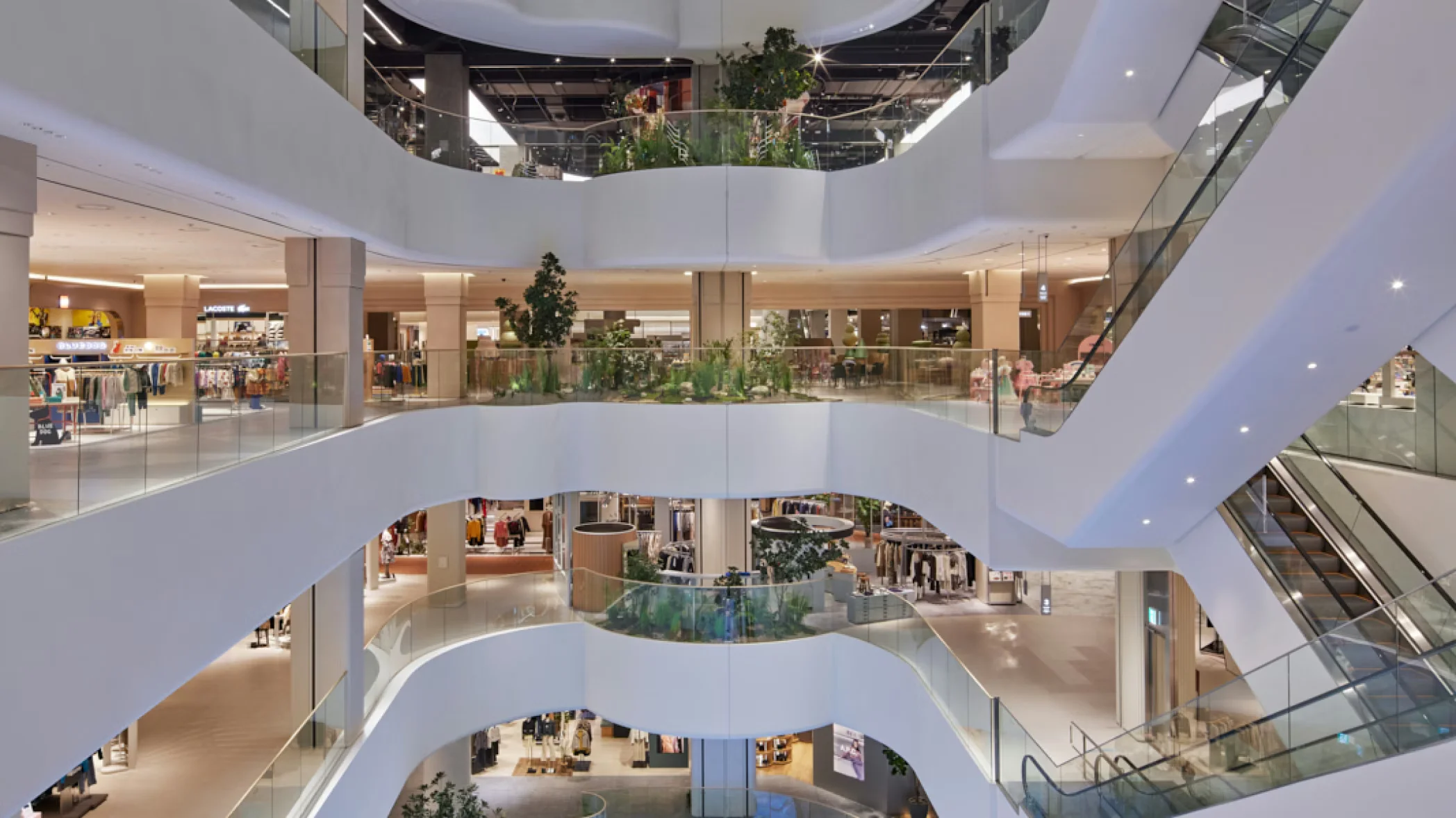 Multi-level commercial interior atrium by Shed with curved white balconies, glass railings, and integrated indoor planting.