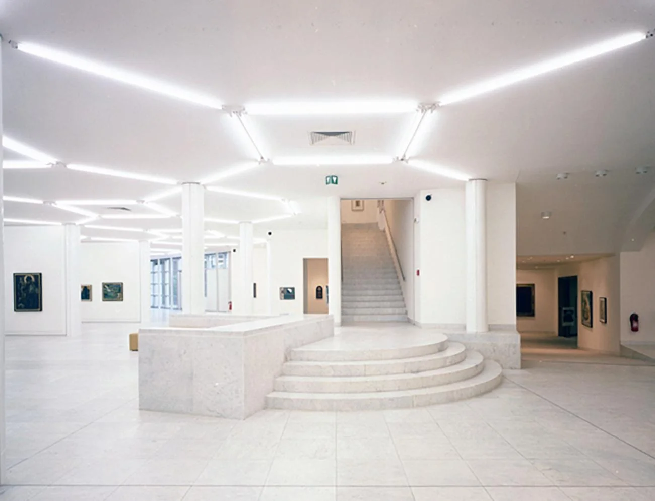 White marble lobby of Museum Abteiberg by Hans Hollein, featuring a hexagonal ceiling light grid and curved steps.