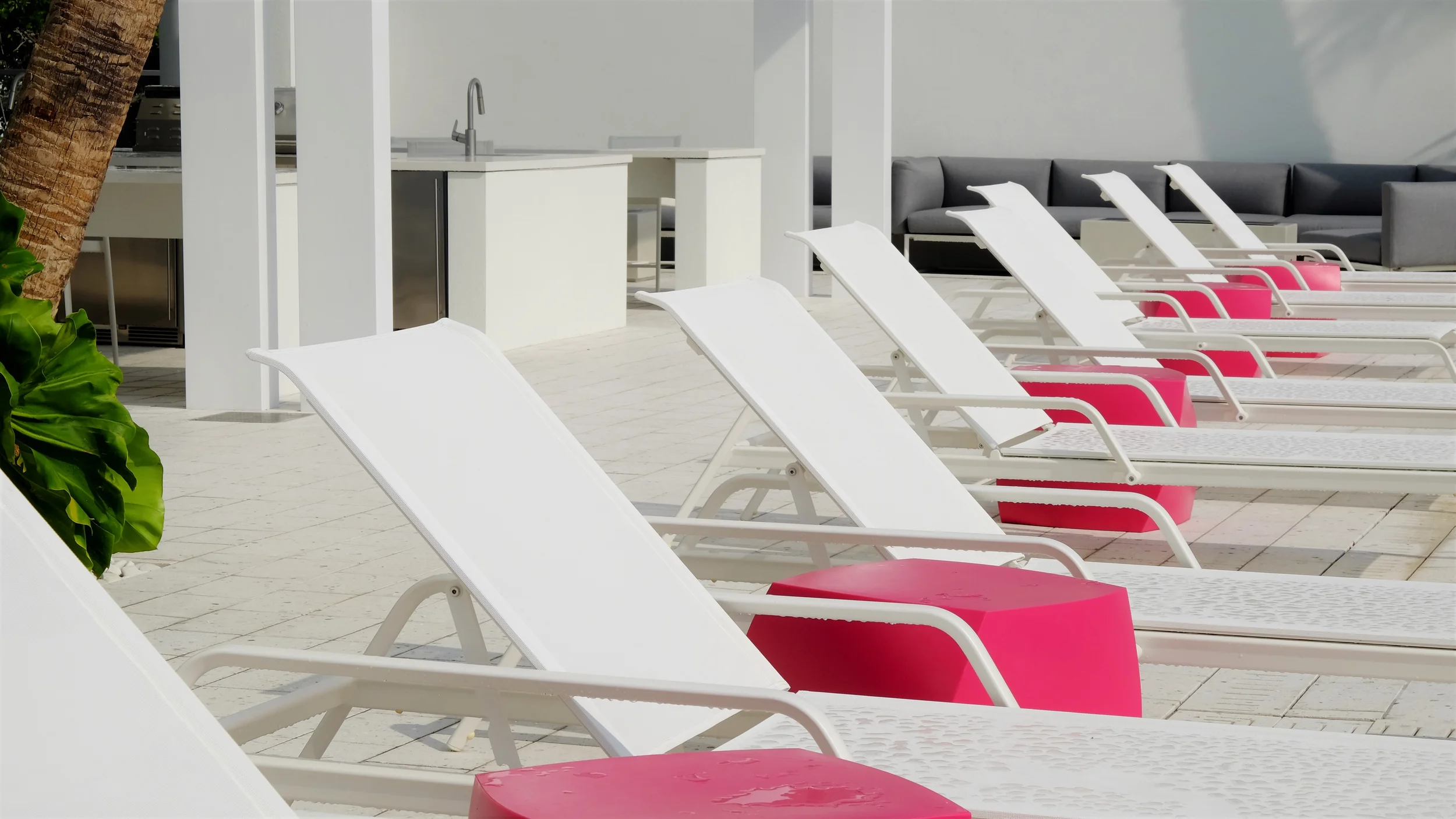 A row of white lounge chairs with bright pink side tables on a white poolside patio by DWY Landscape Architects.