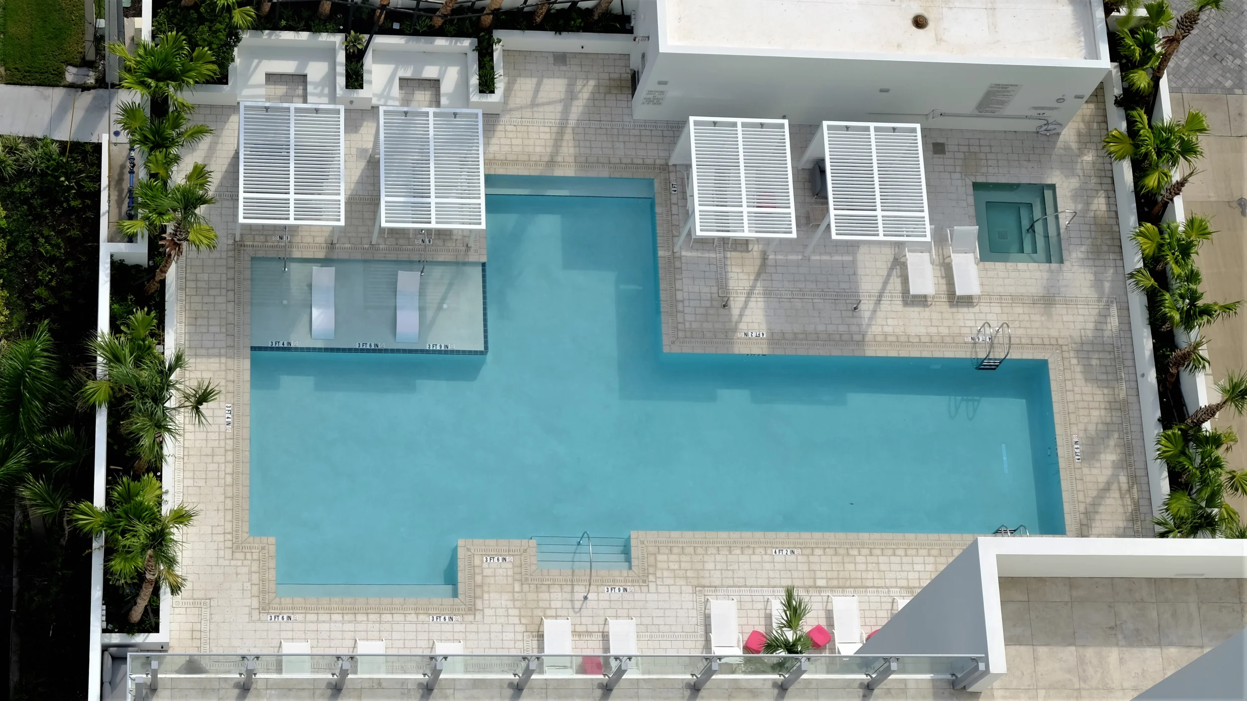 Aerial top-down view of Epoch Sarasota pool deck by DWY Landscape Architects featuring white cabana structures, loungers, and pale stone paving.