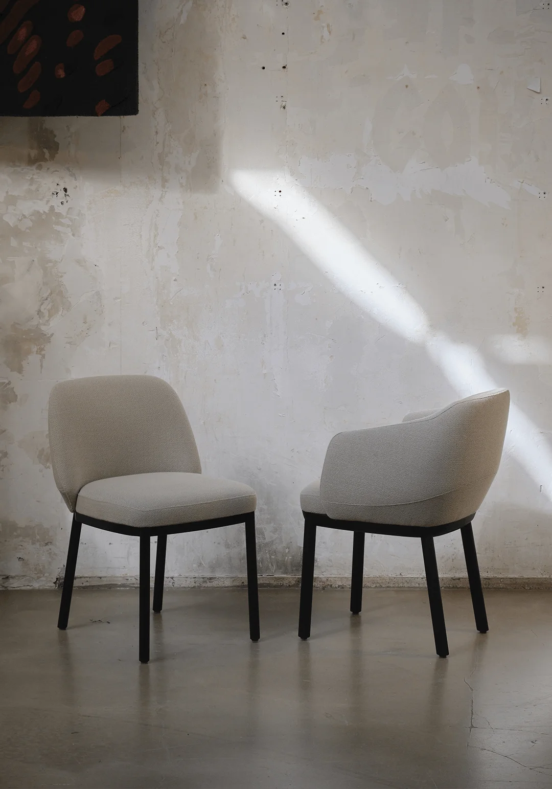 Two upholstered armchairs with dark thin legs placed against a distressed white plaster wall by Jouin Manku.