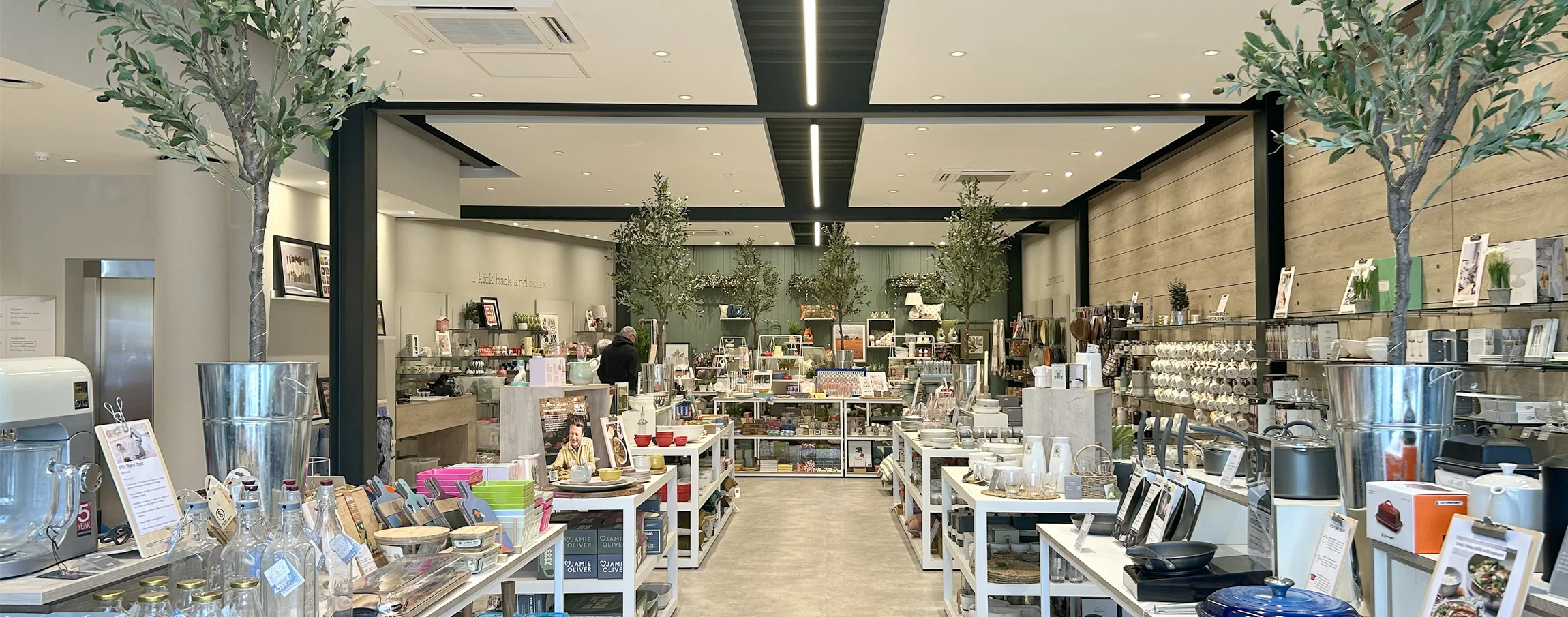 Retail store interior with display tables, central walkway, and suspended drop ceiling panels by Creative SPARC Architects.