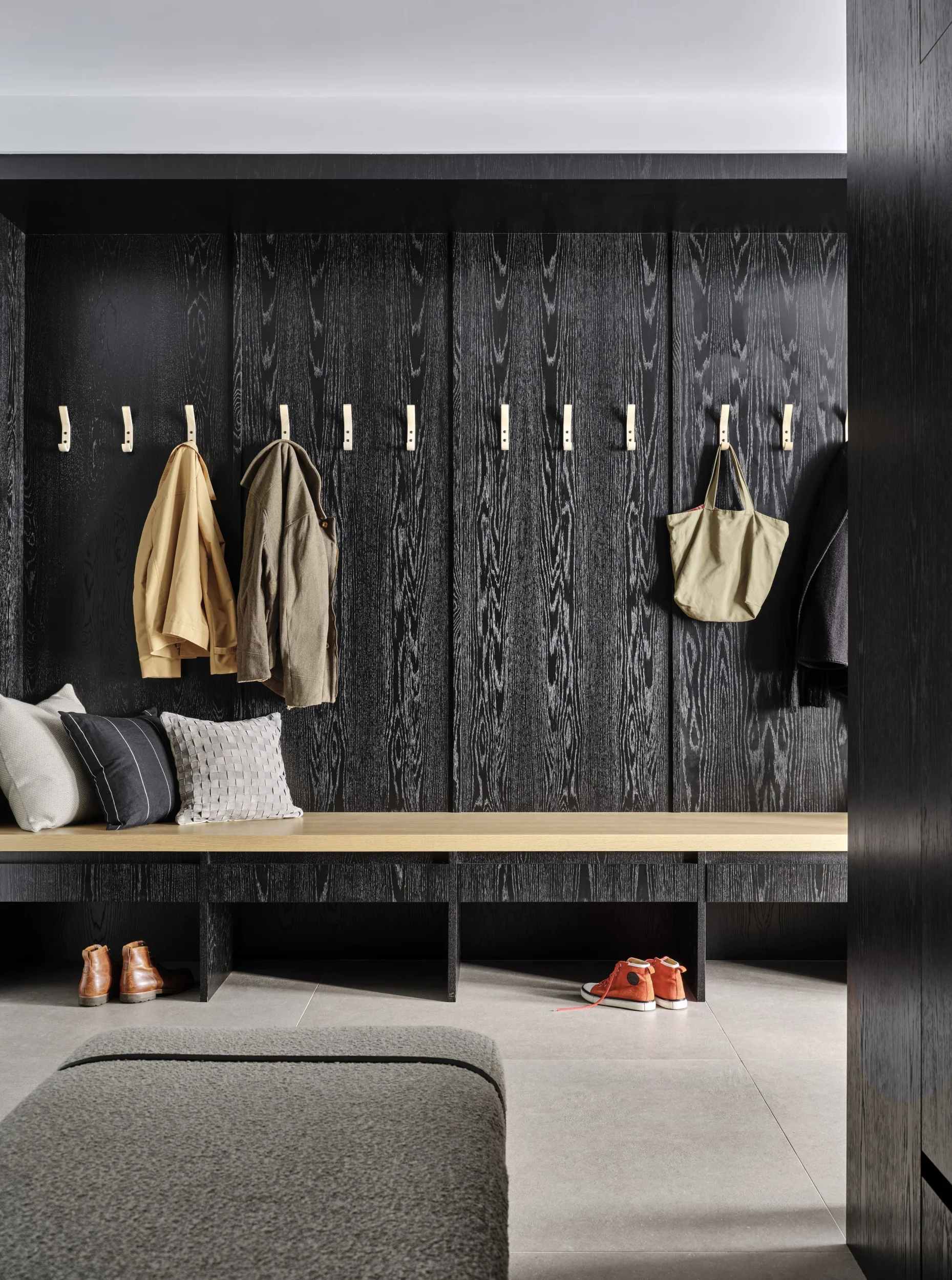Built-in black stained wood mudroom bench with light wood seat and hooks by Chango & Co.