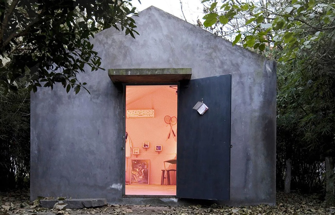 The Hu Huishan Memorial by Liu Jiakun, a small gabled concrete pavilion with an open door revealing a warm pink interior.