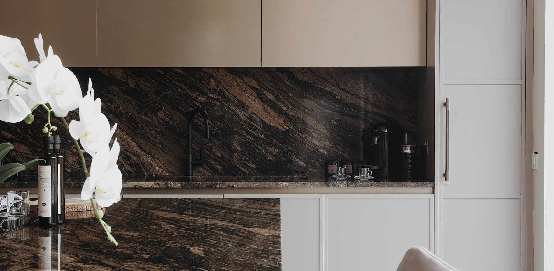 Contemporary kitchen with dark brown marble worktops, bronze upper cabinets, and white lower cabinetry by The Wood Works.