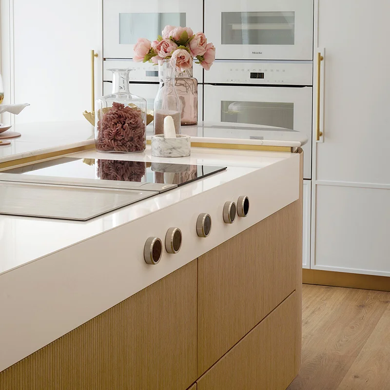 Detailed interior kitchen island by The Wood Works with fluted wood cabinetry, white stone countertop, and integrated round controls.