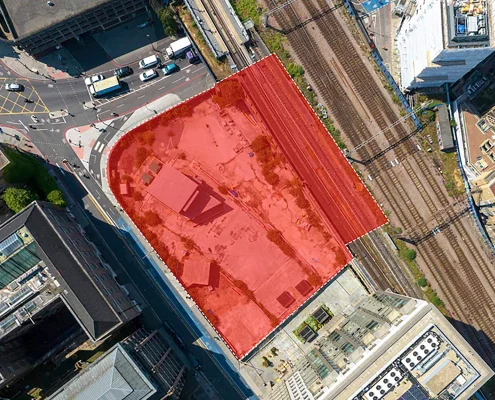 Aerial site photo with a red overlay boundary marking the Royal Mint Gardens project site adjacent to railway tracks and urban streets.