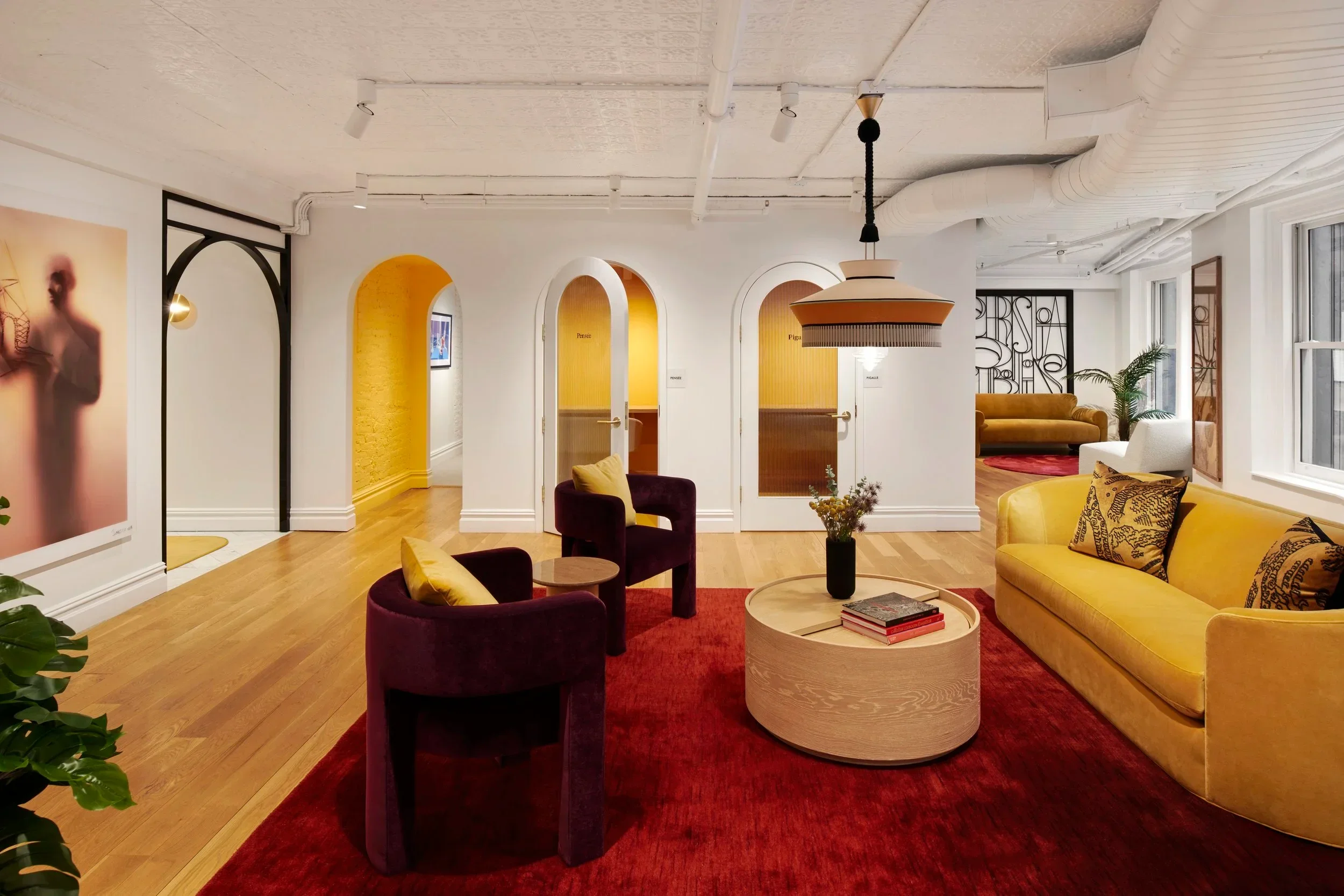 Interior lounge with a yellow sofa, velvet armchairs, arched doorways, and exposed ceiling infrastructure by Alda Ly Architecture.