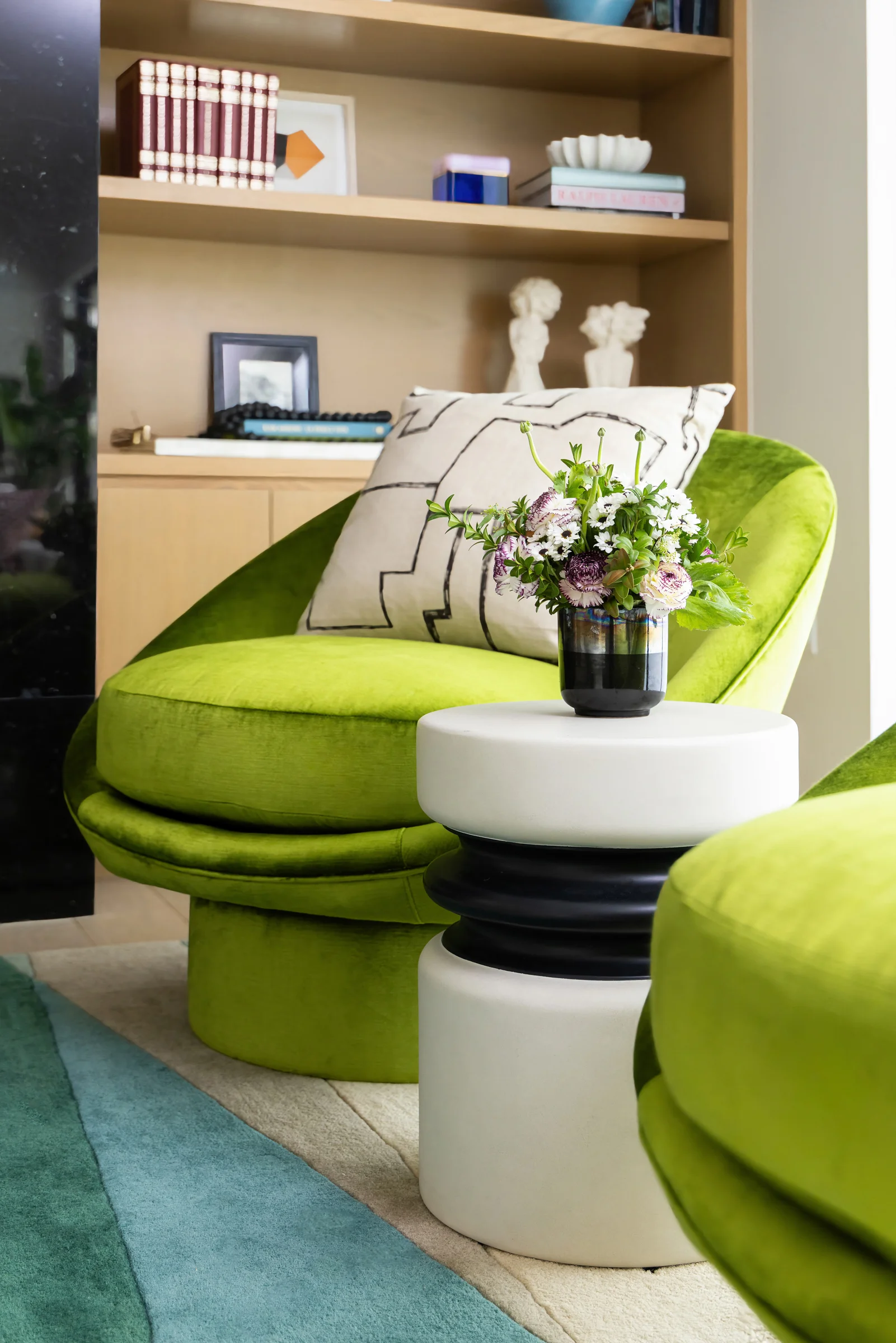 A vibrant green velvet lounge chair paired with a white and black side table in a contemporary living space by Laura U Design Collective.