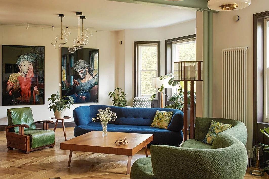 Living room interior with blue and green curved sofas, timber coffee table, herringbone floor, and large artwork by Bradley Van Der Straeten Architects.