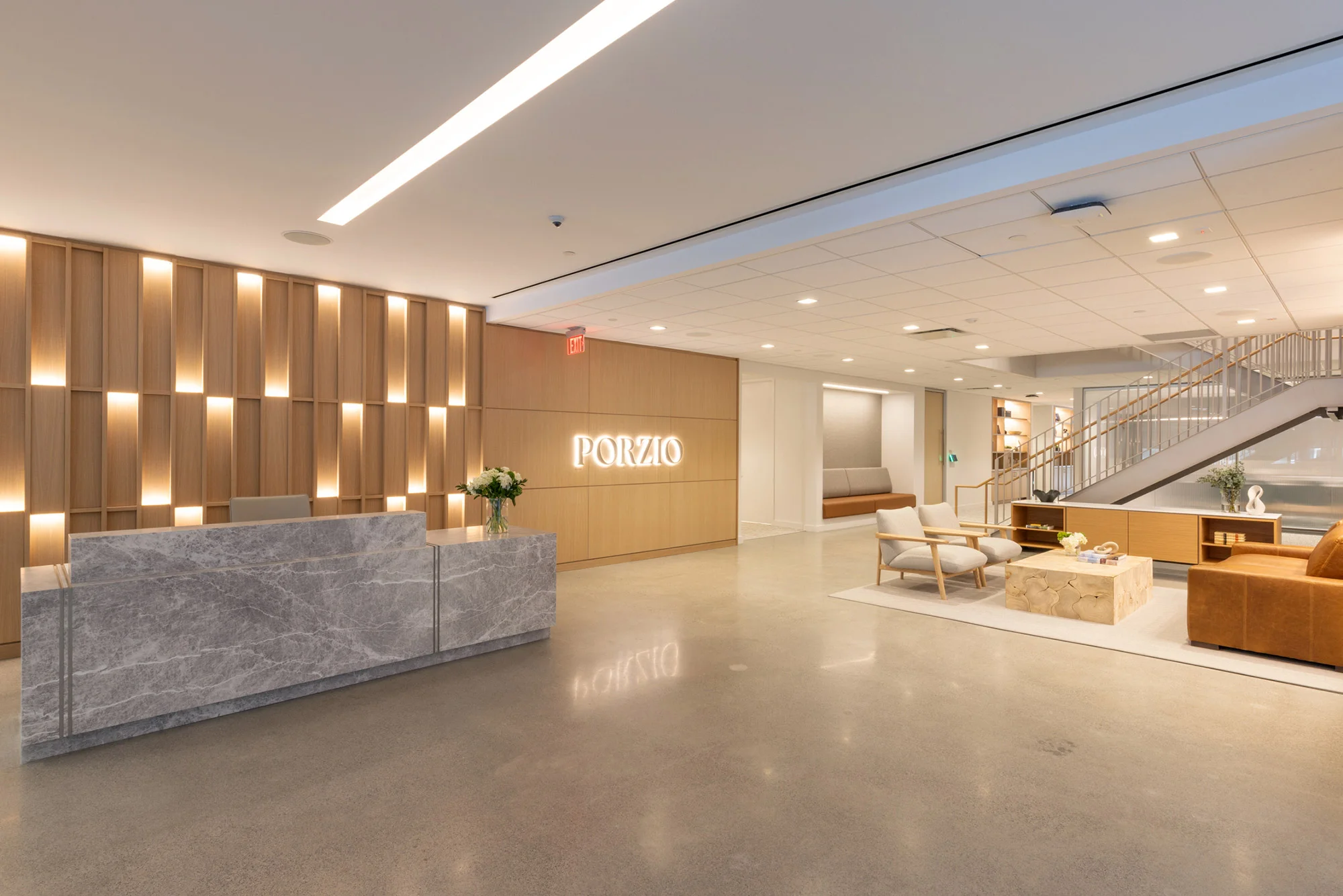 Corporate reception area with a stone reception desk, wood slat wall with backlighting, and polished concrete floor by Studio 1200.