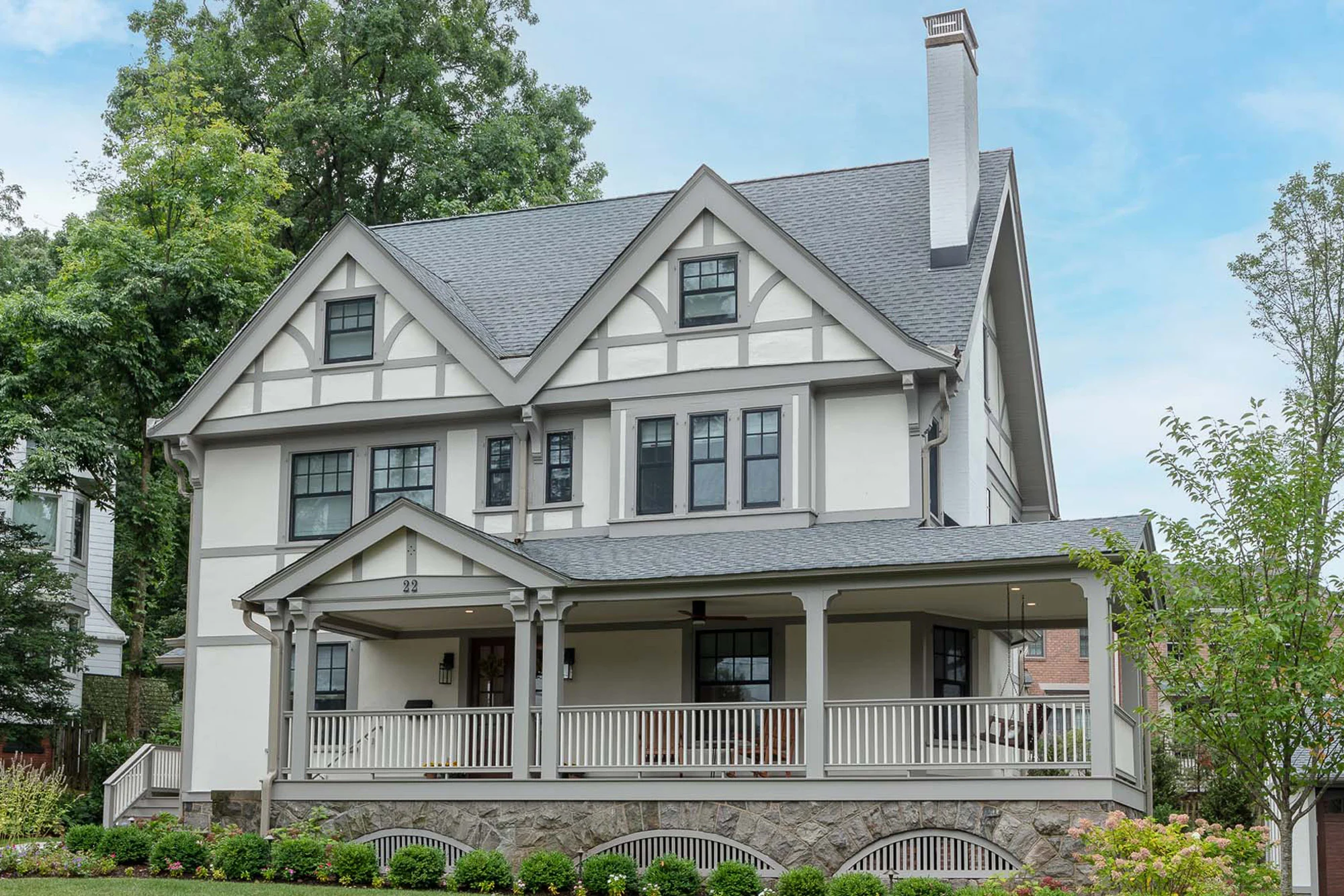 Exterior facade of Summit Residence featuring a wraparound porch, half-timbering details, and a stone foundation by Studio 1200.