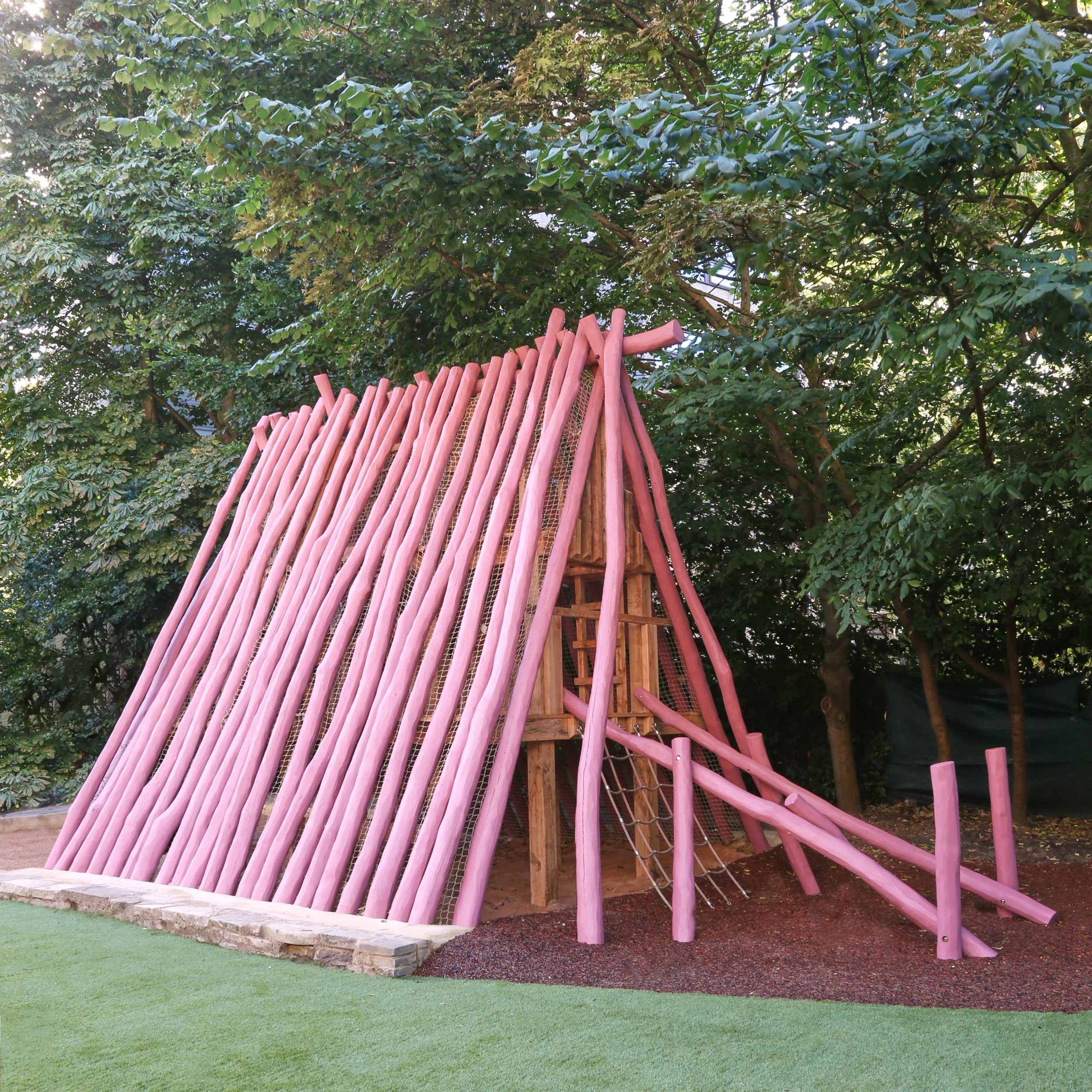 Miss Daisy playground structure by House of Kin featuring an A-frame design with pink-painted rustic log cladding and rope netting.