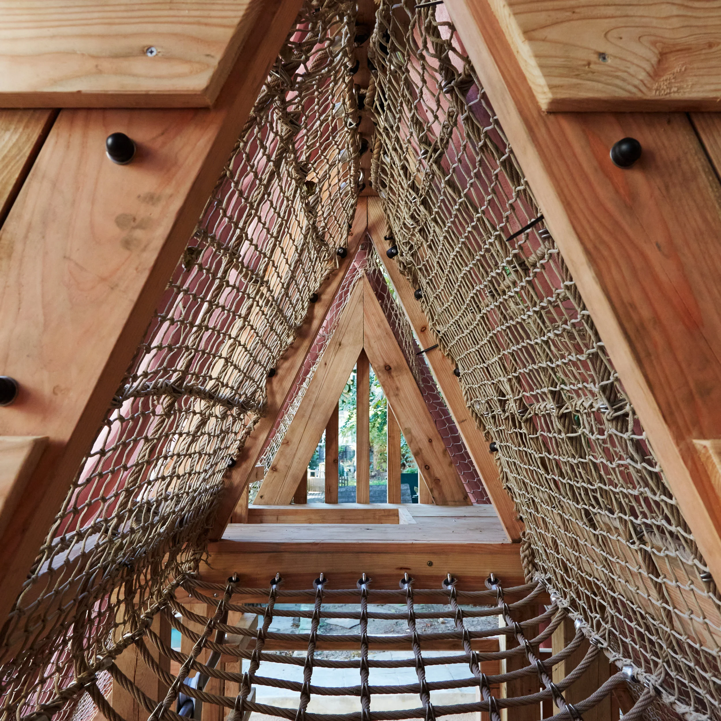 A-frame timber play structure interior featuring layered climbing nets and wooden framing by House of Kin.