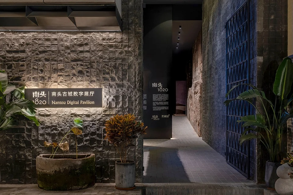 Textured slate stone wall with illuminated signage next to a dark narrow corridor at Nantou Digital Pavilion by 一十一建筑.