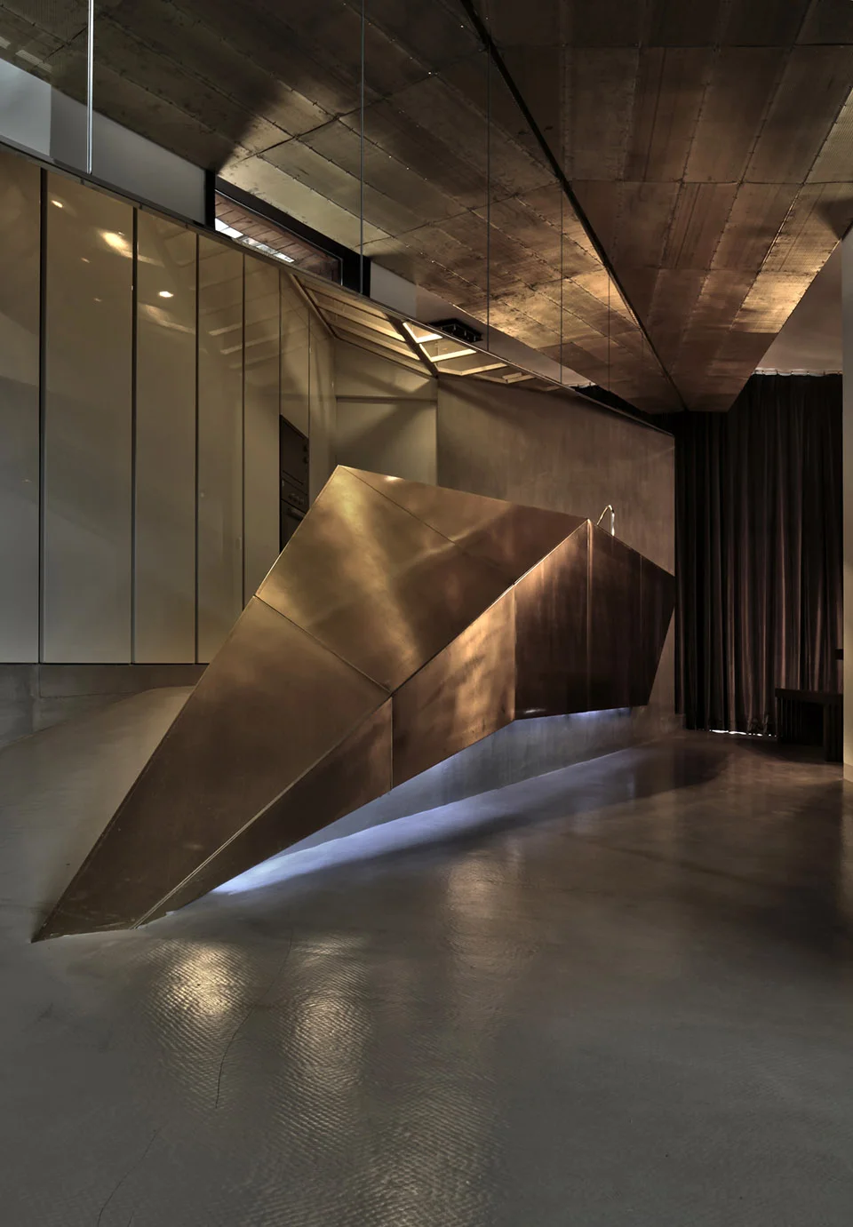 Faceted metallic sculptural island bar in a moody interior with board-formed concrete ceiling by SpActrum.