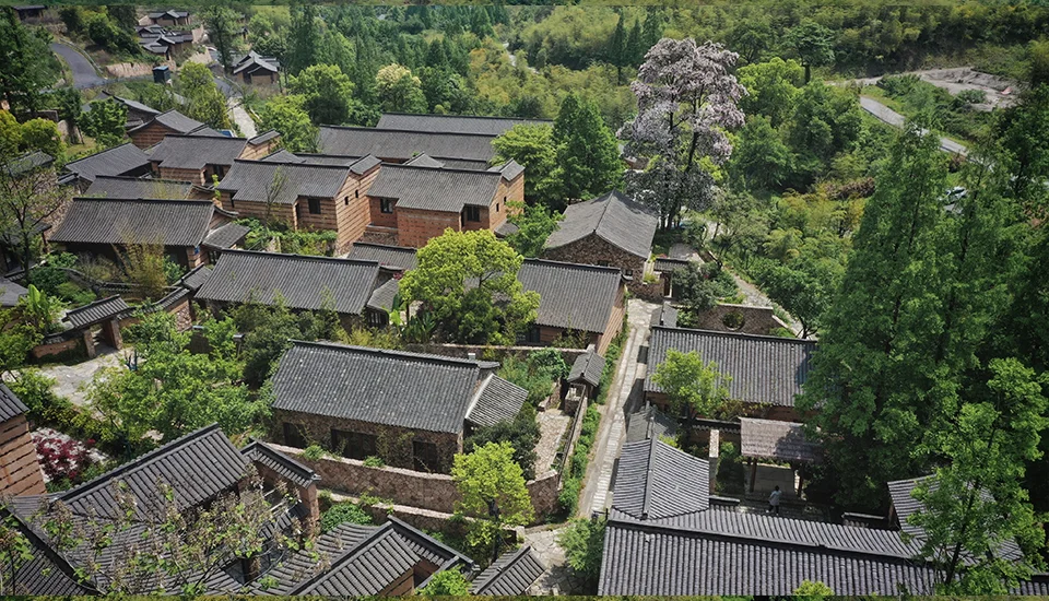 Aerial overview of a mountainside village renovation by 聚石设计 featuring clustered gable-roofed buildings with dark tile and stone walls.