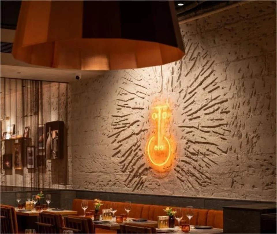 Interior dining space with a textured brick wall featuring a glowing neon light installation and orange banquette seating.