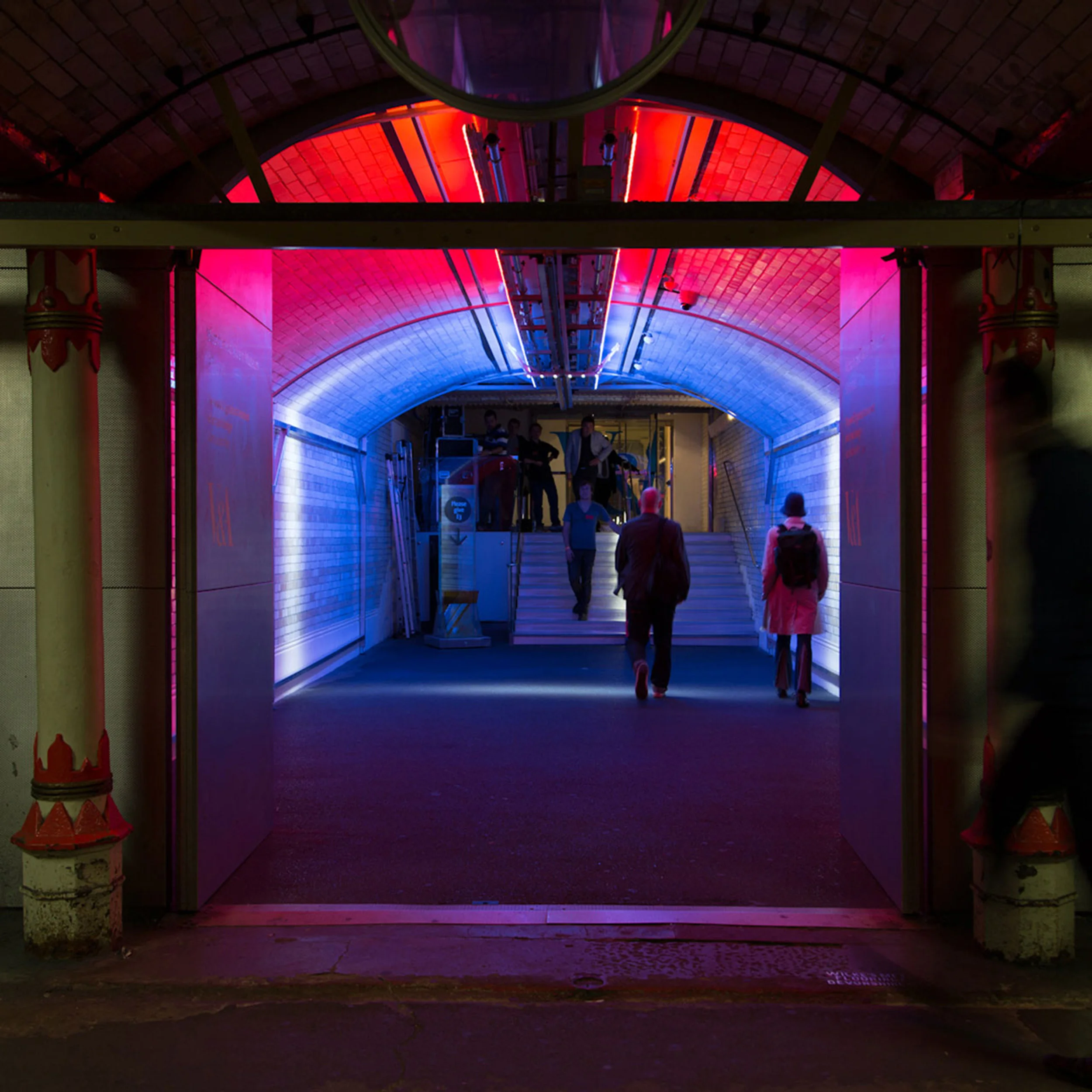V&A tunnel installation featuring vibrant neon red and blue lighting washing vaulted tile ceilings, designed by Cinimod Studio.